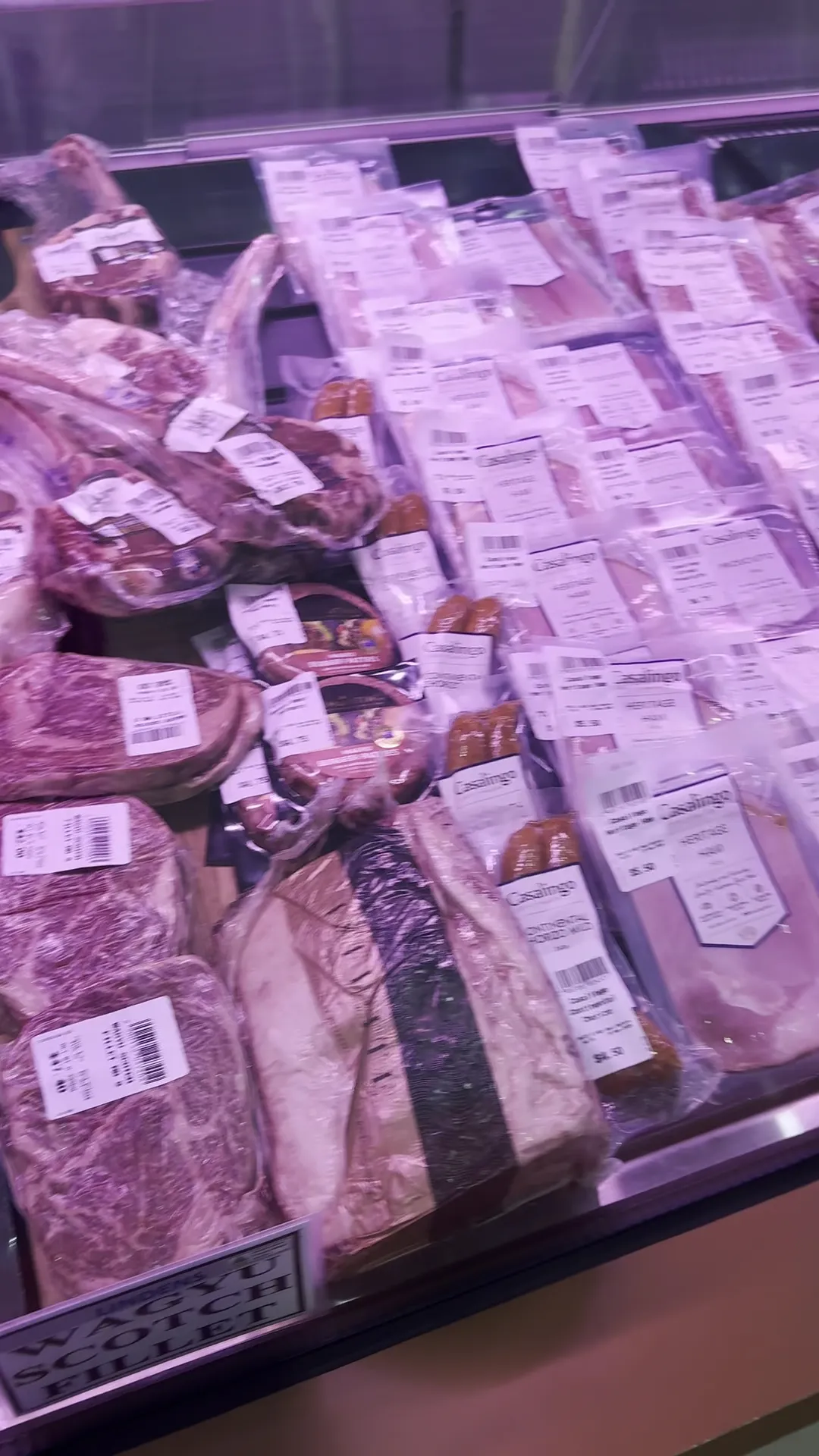 Refrigerated display counter with vacuum-packed beef cuts and whole steaks under pink counter lighting